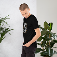 Man wearing a black t-shirt with text, standing between two potted plants against a white wall.