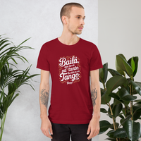 Man wearing a red t-shirt with white text standing between two plants.