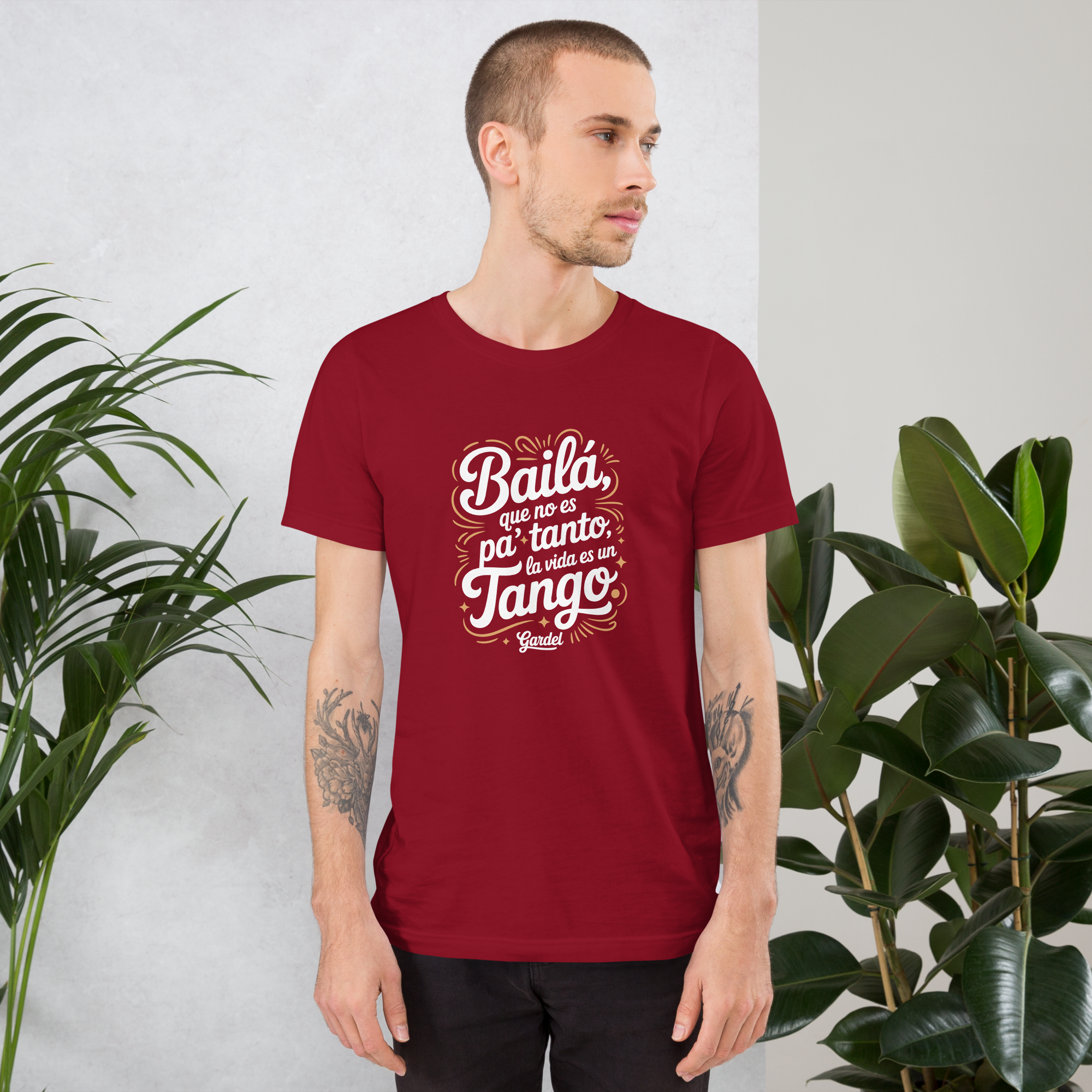 Man wearing a red t-shirt with white text standing between two plants.