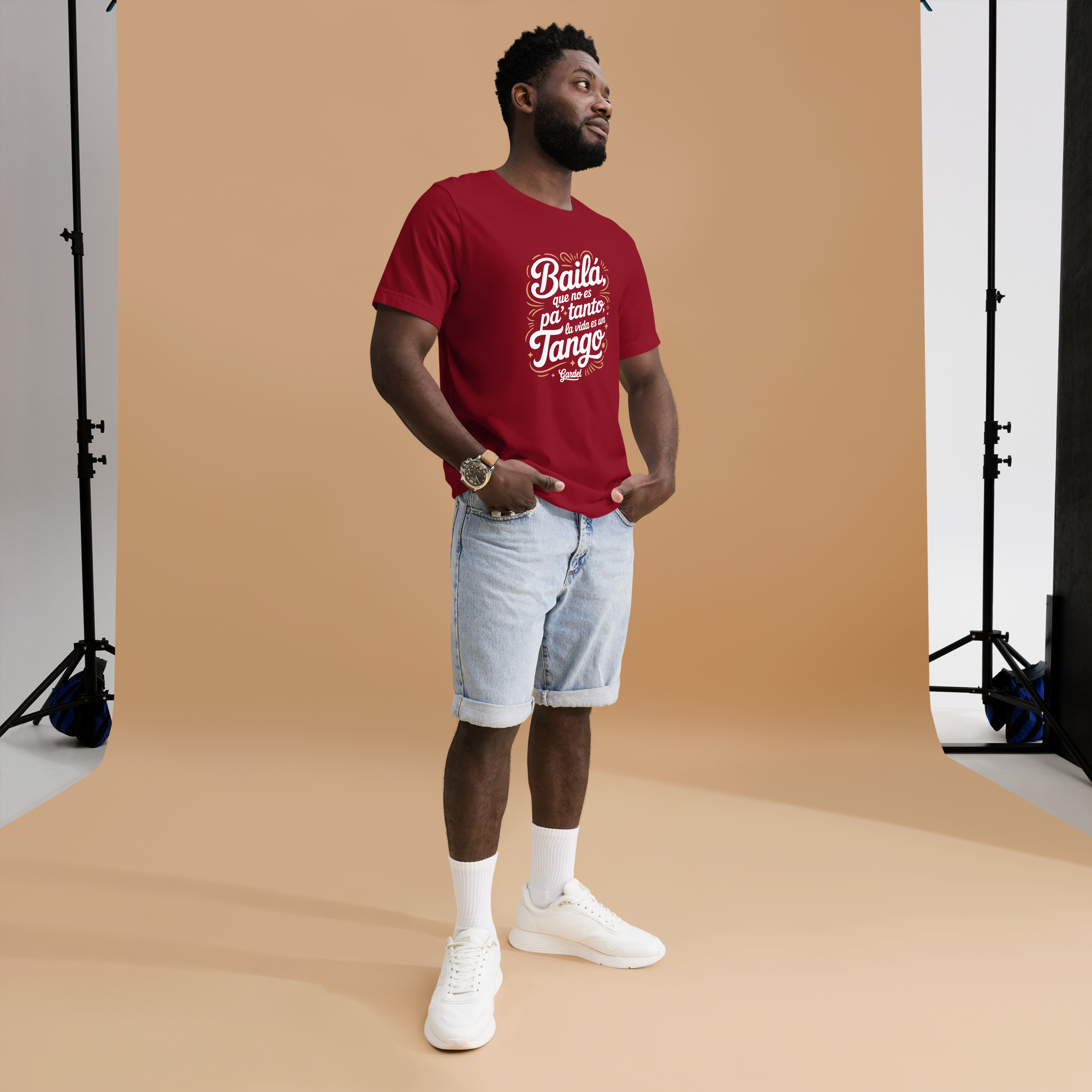 Man wearing a red t-shirt with white text, light blue shorts, and white sneakers in a studio setting.
