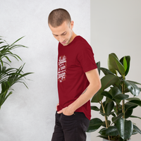 Man wearing a red t-shirt with white text, standing between two potted plants against a white wall.