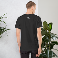 Man wearing a black t-shirt with text on the back, standing against a light gray wall with plants.