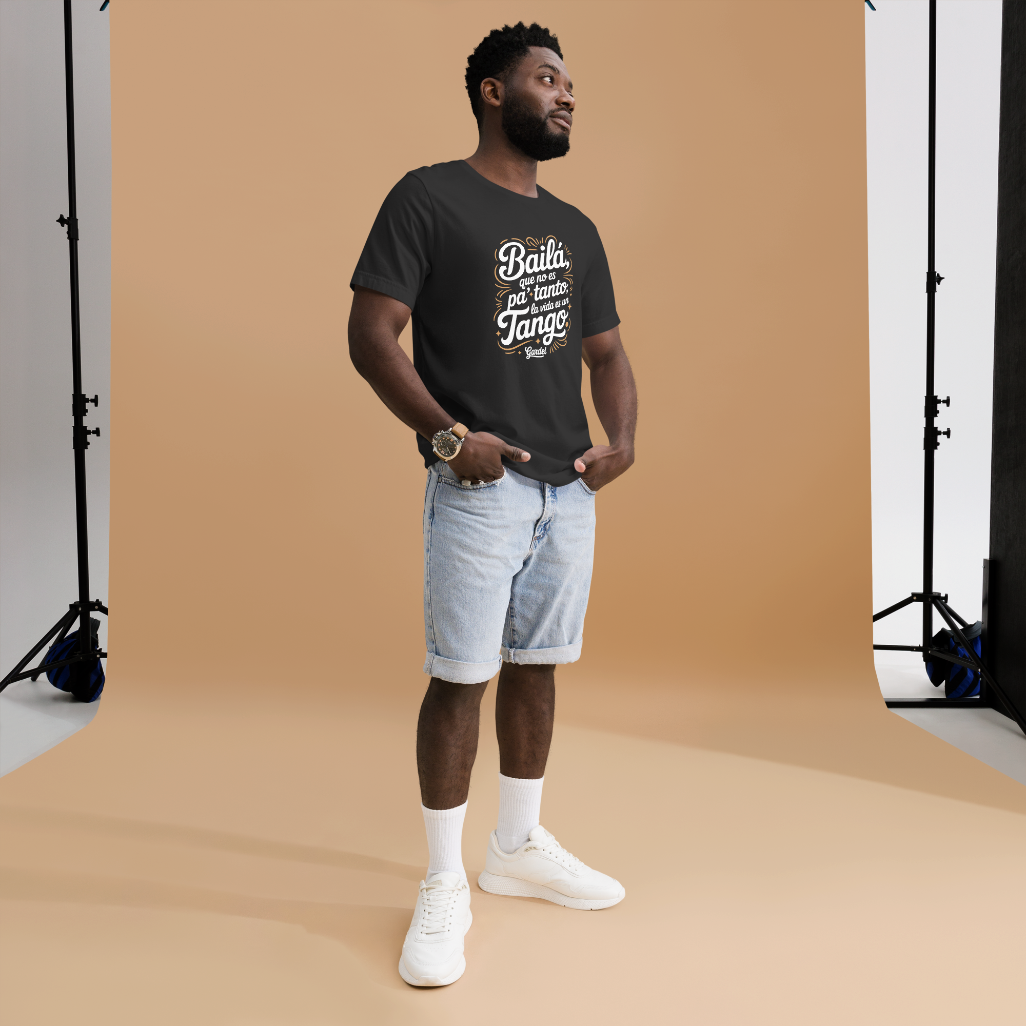 Man wearing a black t-shirt with text and light blue shorts standing in front of a brown backdrop.