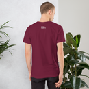 Person wearing a maroon t-shirt with a logo on the back, standing in front of a white wall with plants.