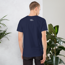 Man wearing a navy blue t-shirt with text on the back, standing against a light gray wall with plants.