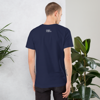 Man wearing a navy blue t-shirt with text on the back, standing against a light gray wall with plants.