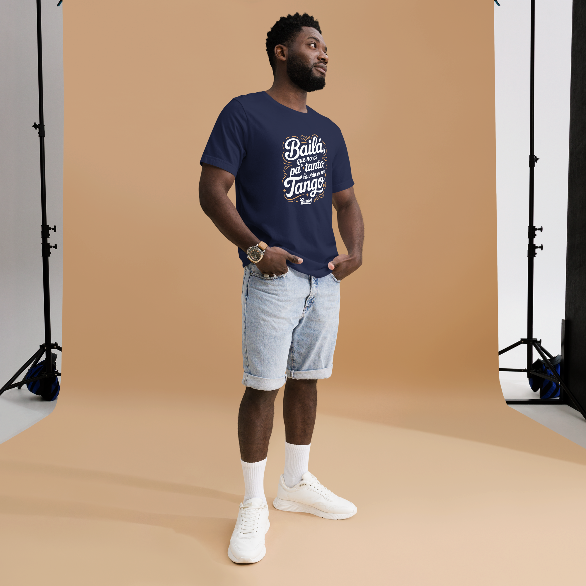 Man wearing a navy blue t-shirt with white text and light blue shorts standing against a brown backdrop.