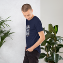 Man wearing a navy blue t-shirt with text, standing between two potted plants against a white wall.