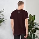 Man wearing a dark brown t-shirt with a logo on the back, standing against a light gray wall with plants.