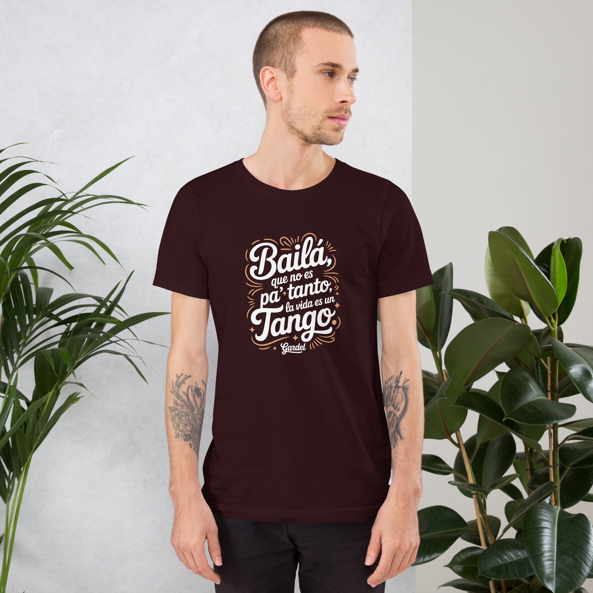 Man wearing a dark brown t-shirt with white text standing in front of green plants.