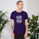 Man wearing a purple t-shirt with text standing between two plants against a light gray wall.