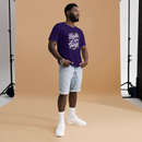 Man wearing a purple t-shirt with text and light blue shorts standing against a brown backdrop.