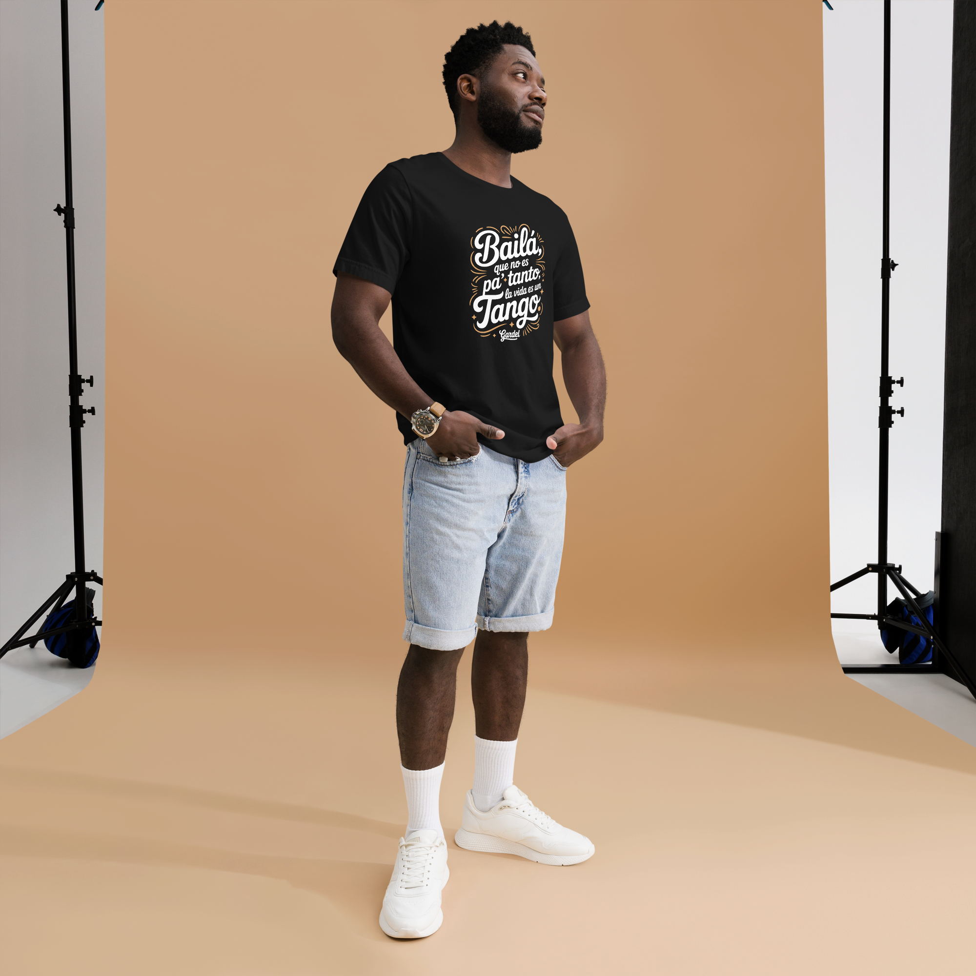 Man wearing a black t-shirt with text and light blue shorts standing in front of a brown backdrop.